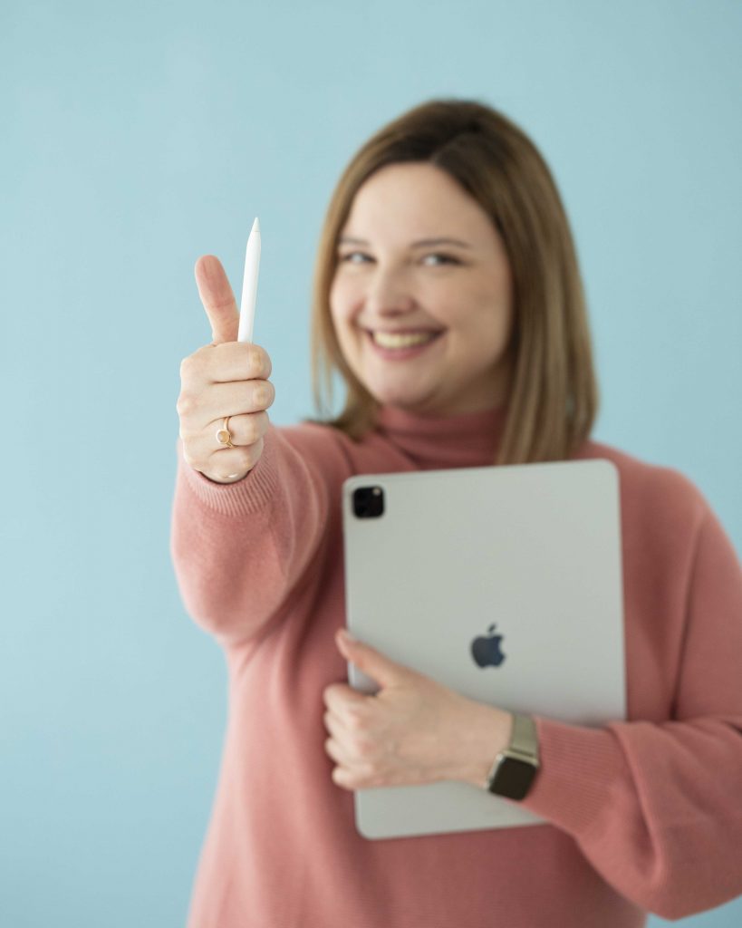 Trainerin mit iPad in einem Arm und einem Apple Pen im anderen ausgestrecktem Arm in der Hand, die einen Daumen nach oben formt